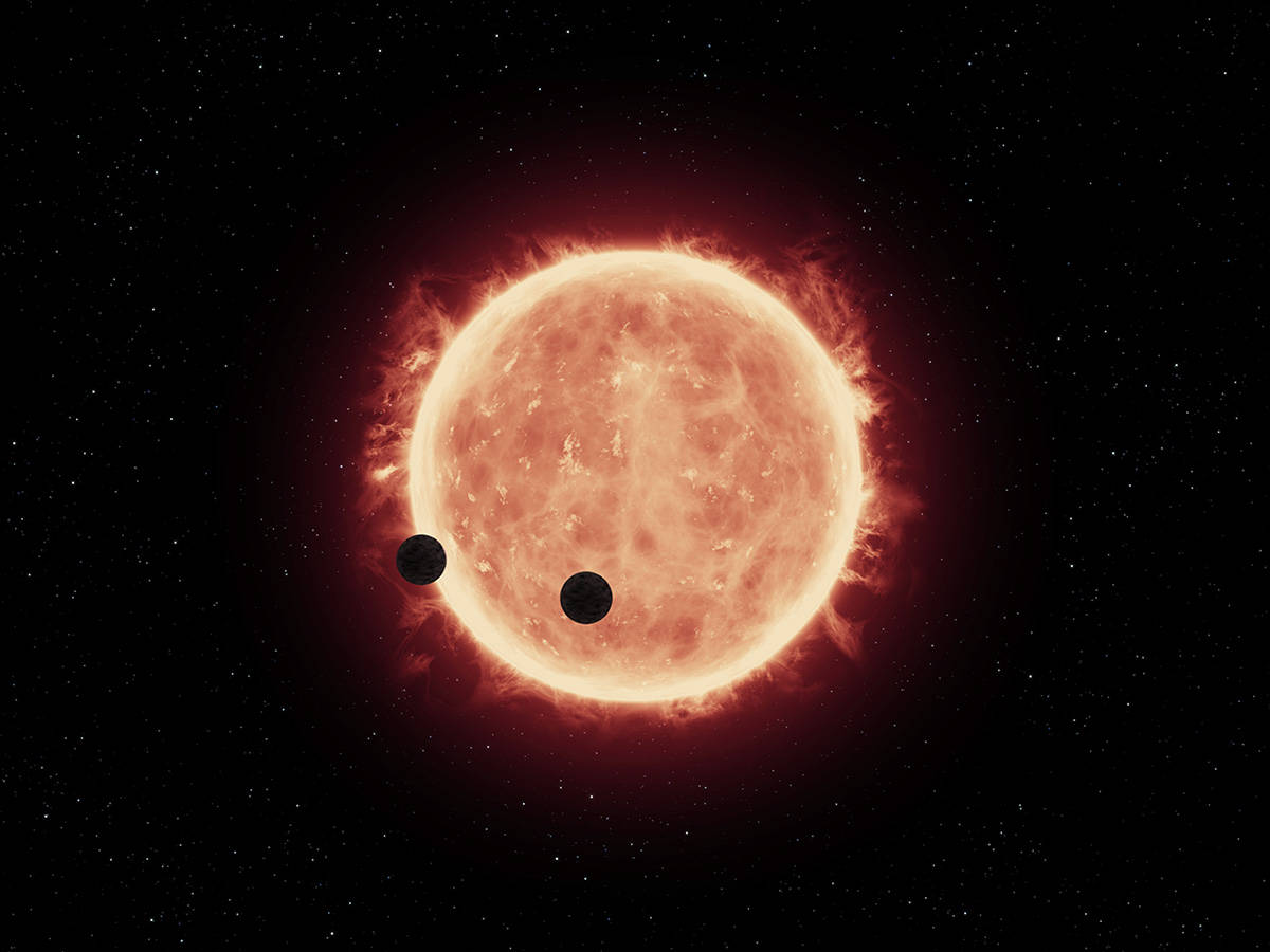 An artist's illustration shows two Earth-sized planets spinning across the face of an M dwarf star called TRAPPIST-1.